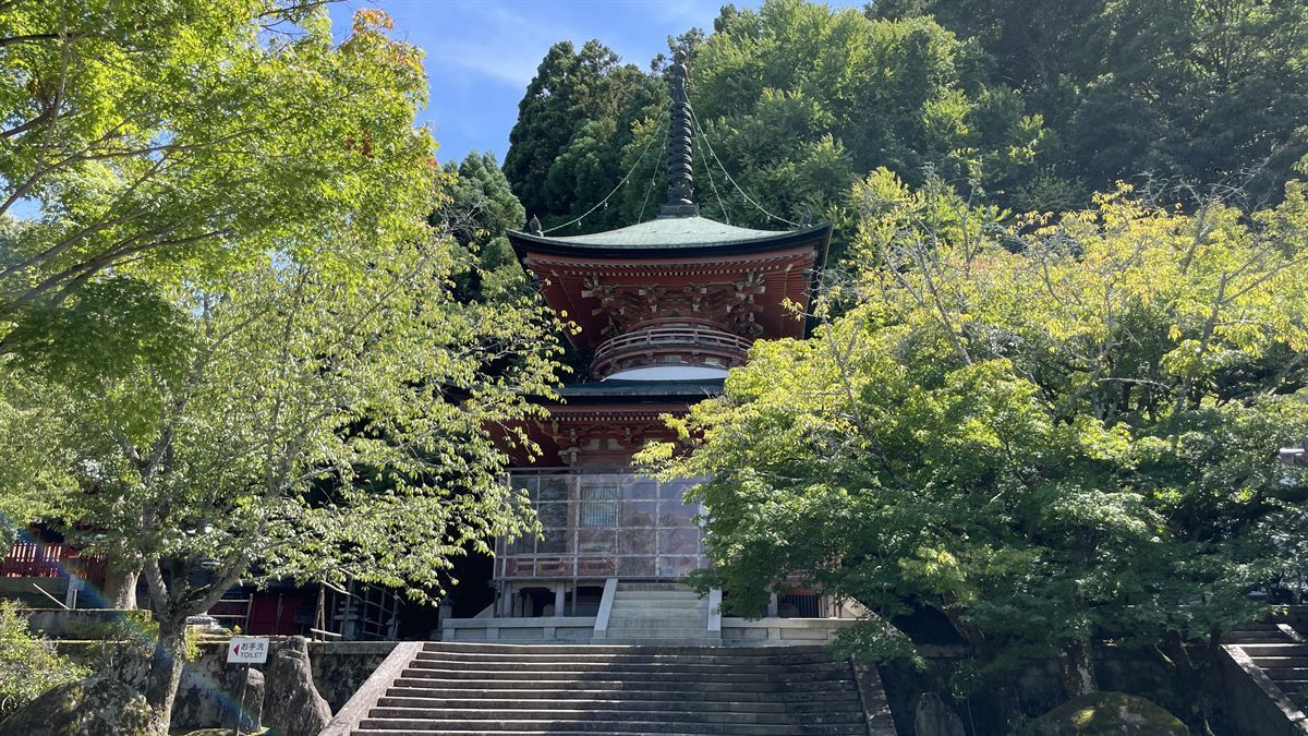 法輪寺の多宝塔。朱塗りの柱と青銅色の屋根、石段の上に青空が広がる