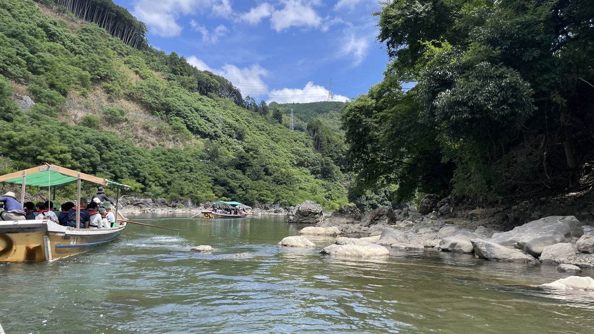 保津川の渓谷。青空の下、竹林の斜面と岩、川面に2艘の舟が浮かぶ