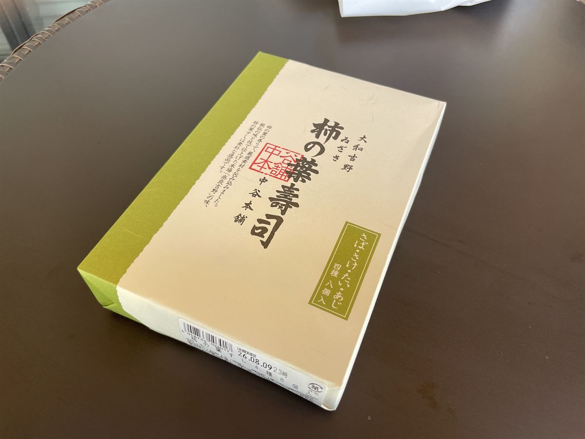 柿の葉寿司の箱。「さば・さけ・たい・あじ 四種 八個入」と印刷され、側面に「消費期限 26.08.09 23時」のラベルが貼られている