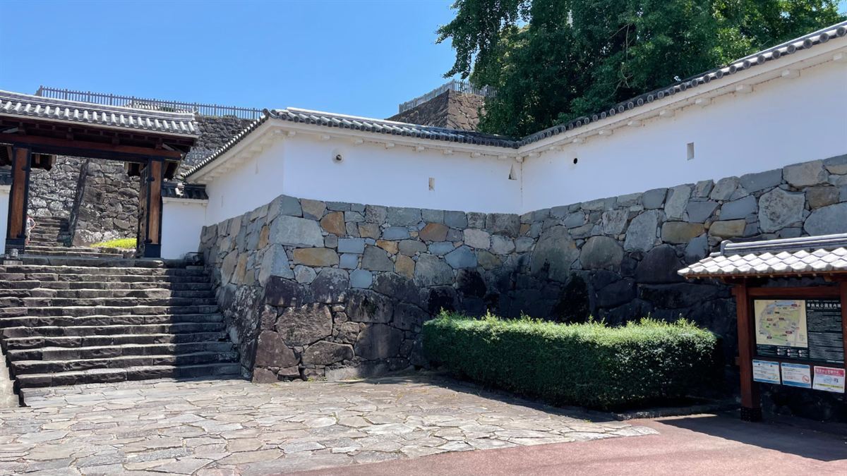 甲府城跡の門と石段、白漆喰の塀と石垣。夏の青空が広がる