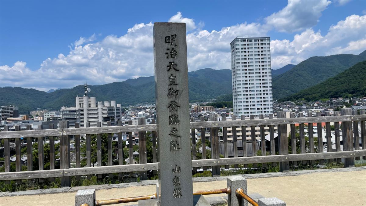 甲府城跡の天守台に立つ「明治天皇御登臨之阯 山梨縣」と刻まれた石碑。奥に甲府の市街地と山並み