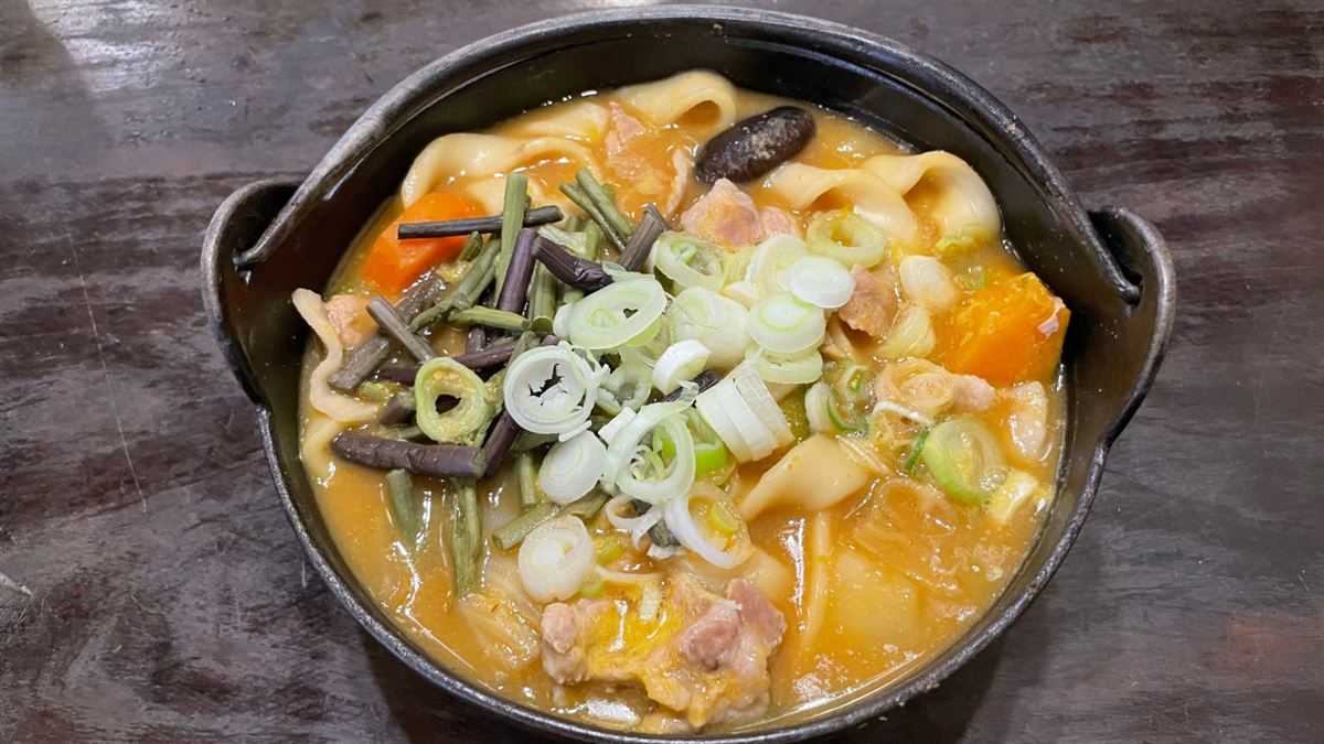 小作の豚肉ほうとうを真上から撮った写真。鉄鍋に平打ちの太麺、豚肉、かぼちゃ、にんじん、しいたけ、山菜、ねぎが入っている