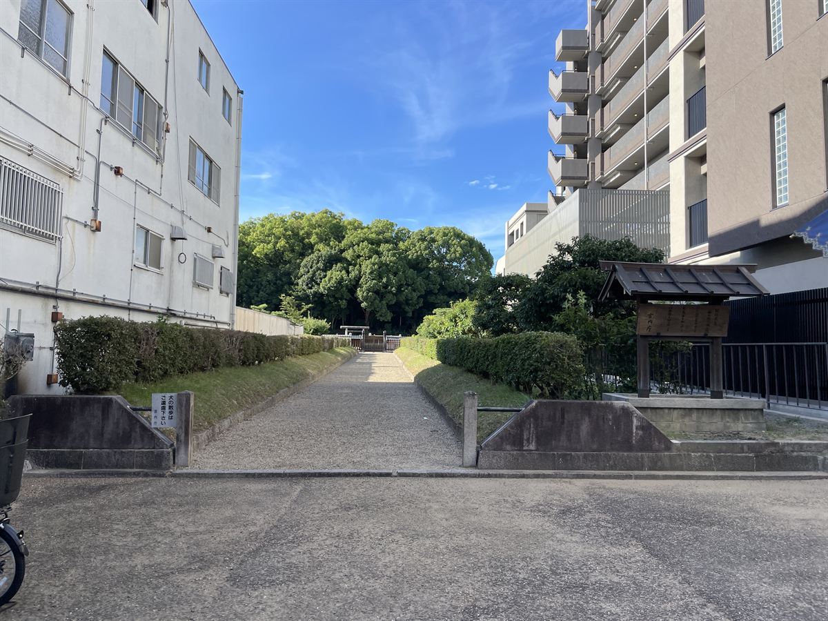 念仏寺山古墳の参道入口。左手にビル、右手にマンション、その間から砂利の参道が奥へ伸びる