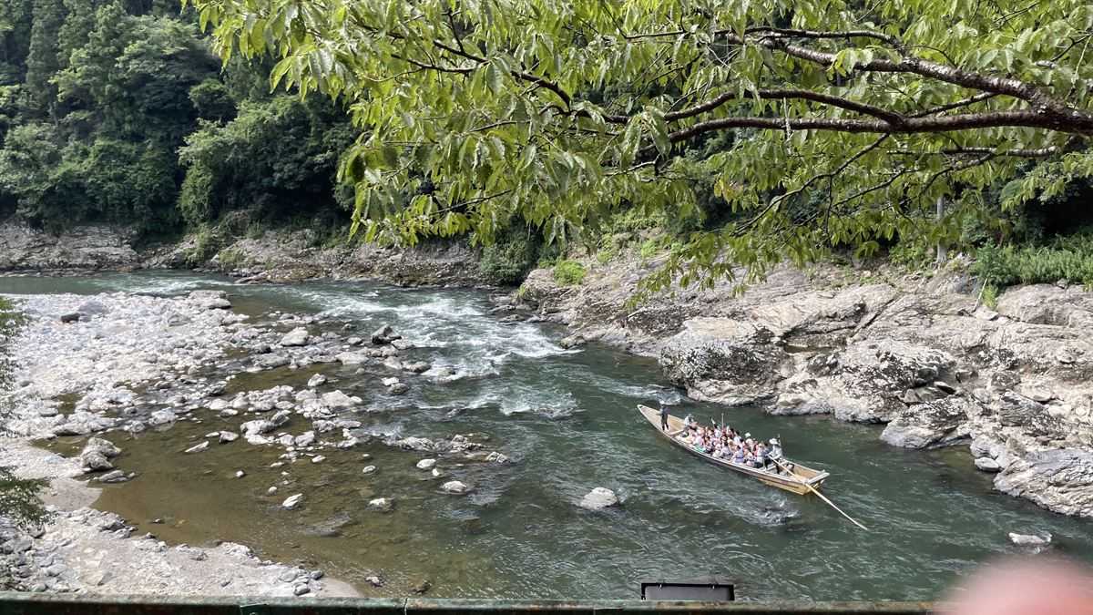 鉄橋の緑の桁ごしに、白波の急流を下る保津川下りの舟