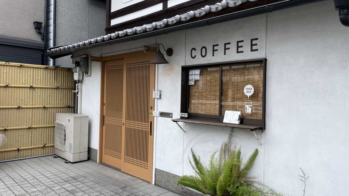 Cafe Januaryの入口。白い壁に「COFFEE」の文字があり、格子の引き戸と小窓がついている
