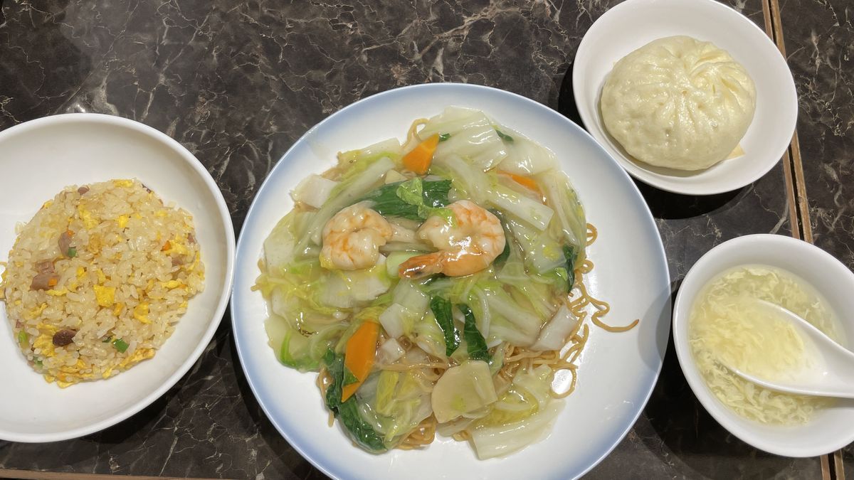 551蓬莱の海鮮焼そばのセット。えびと野菜のあんがかかった焼そばに、炒飯とスープ、豚まんが並んでいる