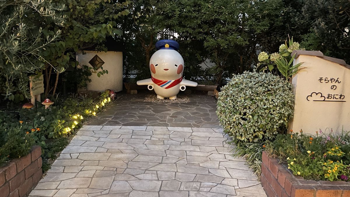 展望デッキの「そらやんのおにわ」。石畳の小道の奥に、帽子をかぶった白い飛行機のキャラクターの像があり、右の壁に「そらやんのおにわ」と書かれている