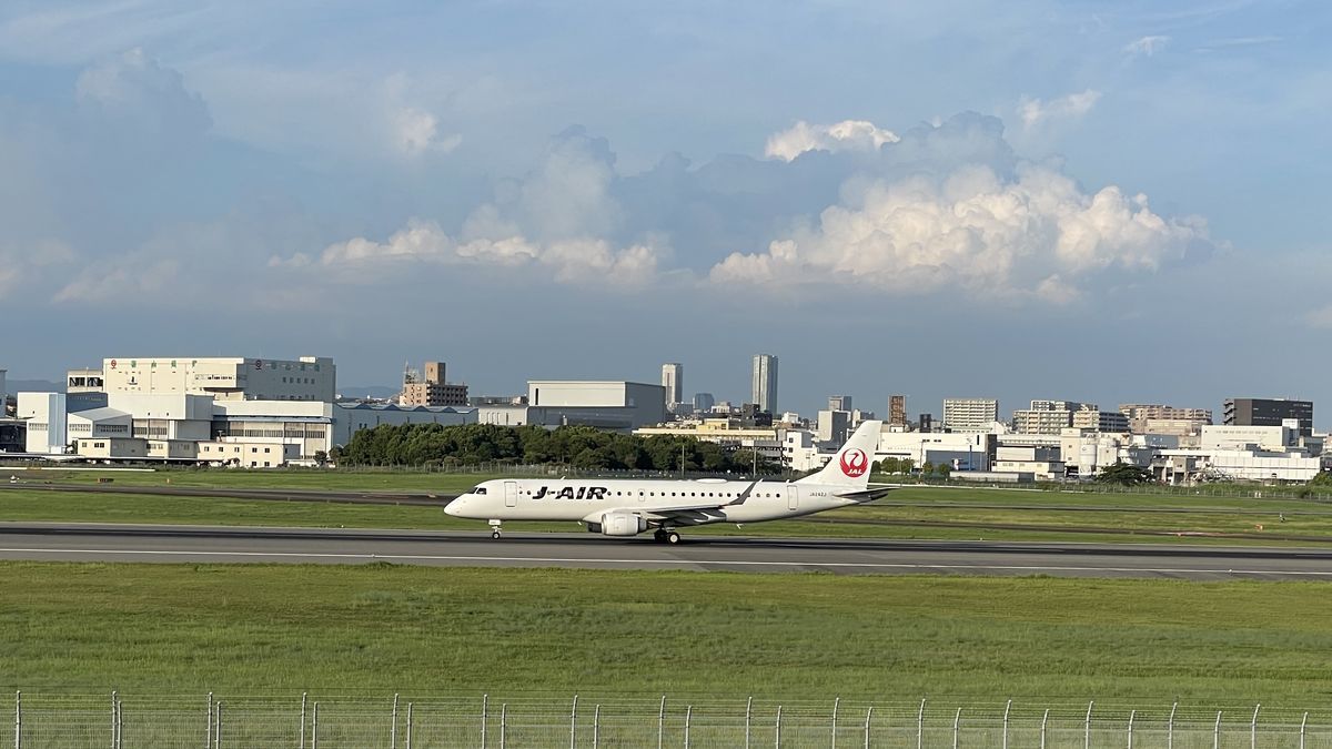 伊丹スカイパークの中央エントランスのあたりから見た、滑走路を走るJ-AIRの飛行機。奥に空港の建物と雲が見える