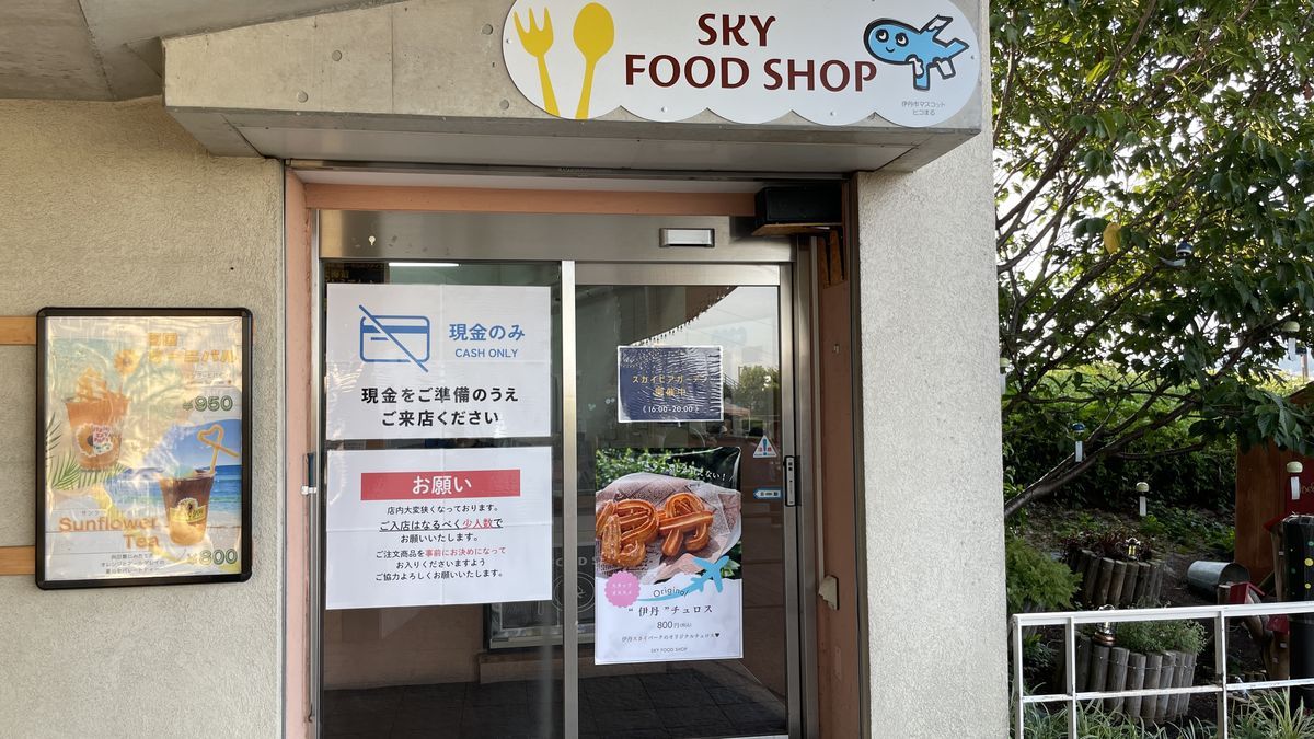 伊丹スカイパークの「SKY FOOD SHOP」の入口。ガラスの扉に「現金のみ」の貼り紙と、スカイビアガーデンの開催中の貼り紙がある