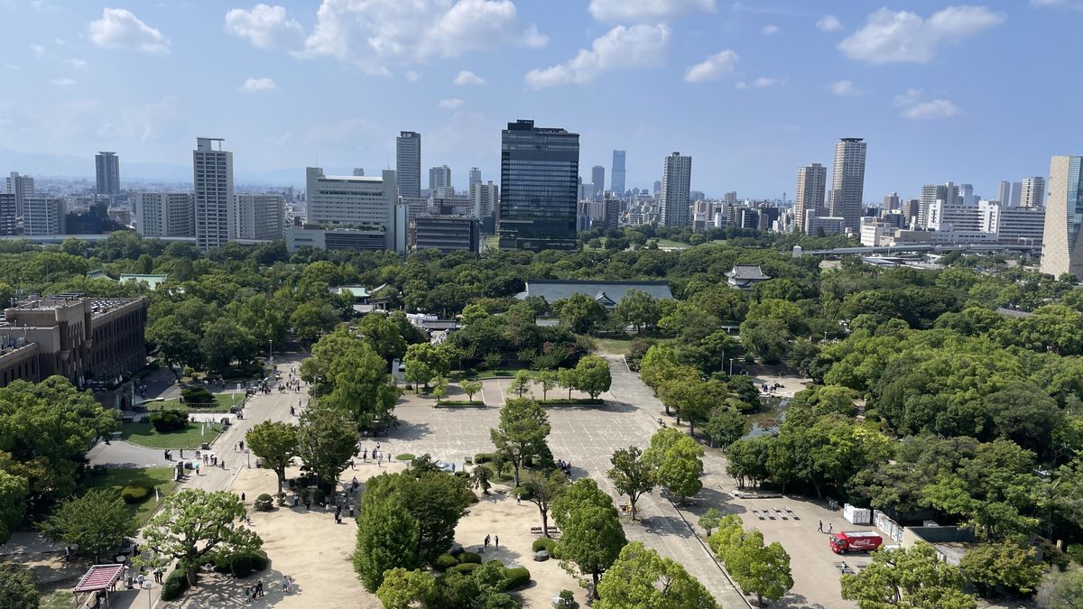 大阪城天守閣8階の展望台からの眺め。公園の緑と大阪市街のビル群の奥に、あべのハルカスが立っている
