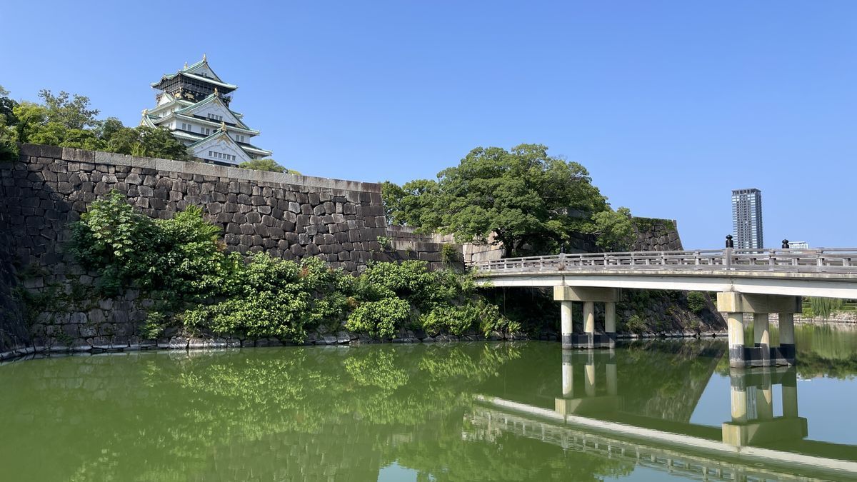 大阪城の内堀にかかる極楽橋と、石垣の上に建つ天守閣。堀の水は緑色をしている