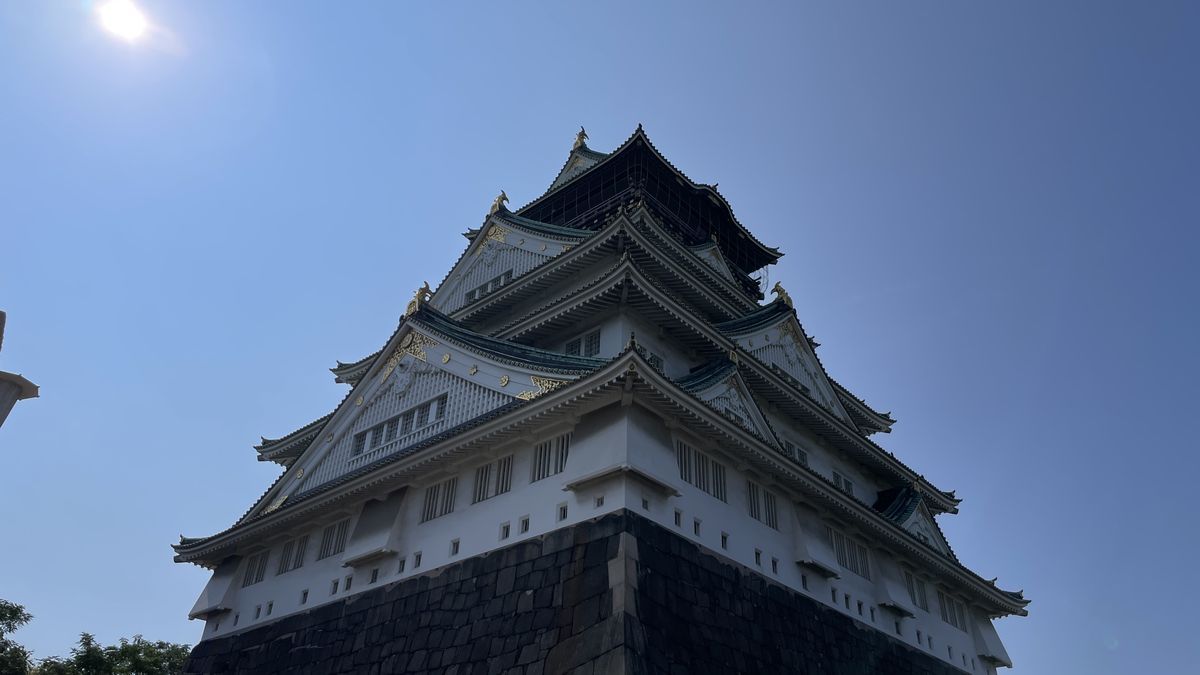 青空を背に、石垣のそばから見上げた大阪城天守閣。白壁と金色の飾りが見えている