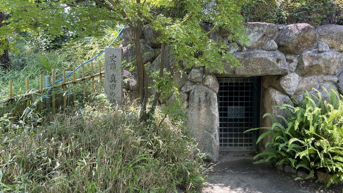三光神社の真田の抜け穴。石組みの入口に鉄格子の扉が閉まっていて、左に史跡の石柱が立っている