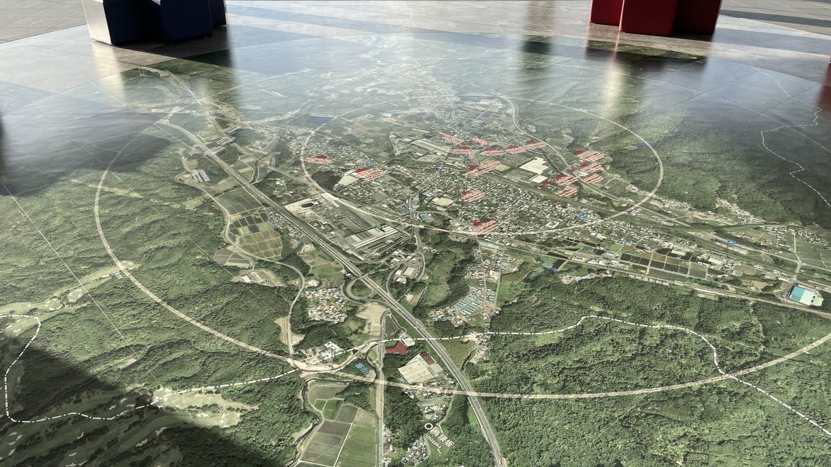 展望室の床に広がる大きな航空写真の地図。陣跡などの場所に赤い札が付き、奥に赤と青の腰かけがある