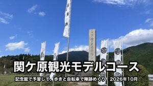 決戦地の石碑と、風になびく白いのぼり。うしろに山と青空が見え、下に「関ケ原観光モデルコース」「記念館で予習して、歩きと自転車で陣跡めぐり　2026年10月」の文字が入っている