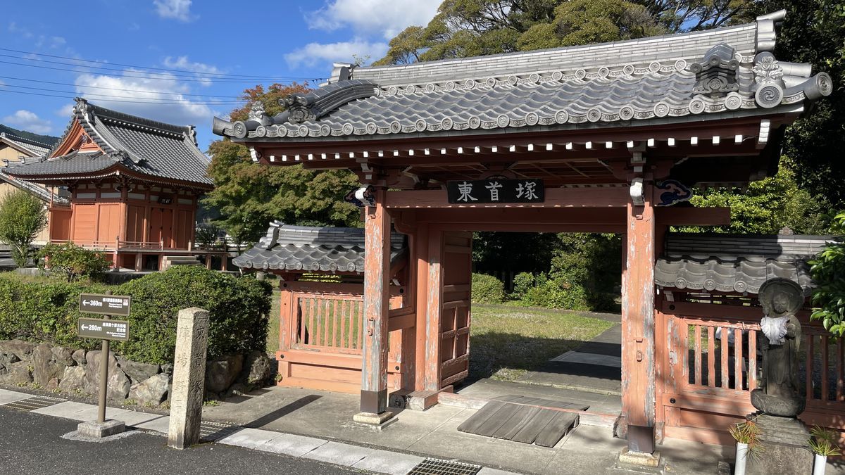 東首塚の朱色の門。瓦屋根の門に「東首塚」の額がかかり、左に朱色のお堂が見える