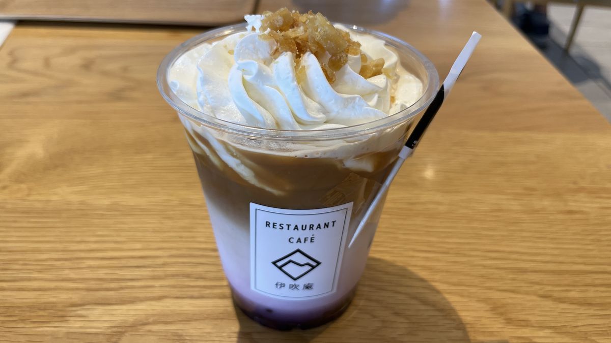 伊吹庵のカップに入った紫芋のラテ。ホイップクリームの上に茶色のトッピングがのり、下のほうが紫色になっている