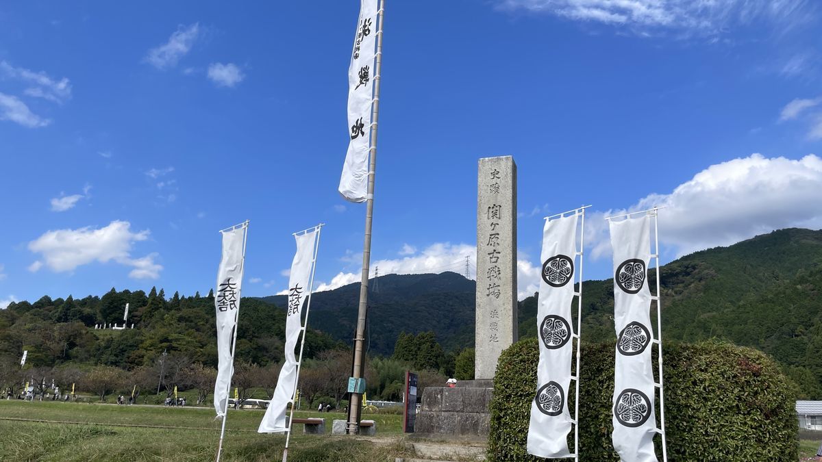 決戦地の石碑と、風になびく白いのぼり。うしろに山と青空が見える