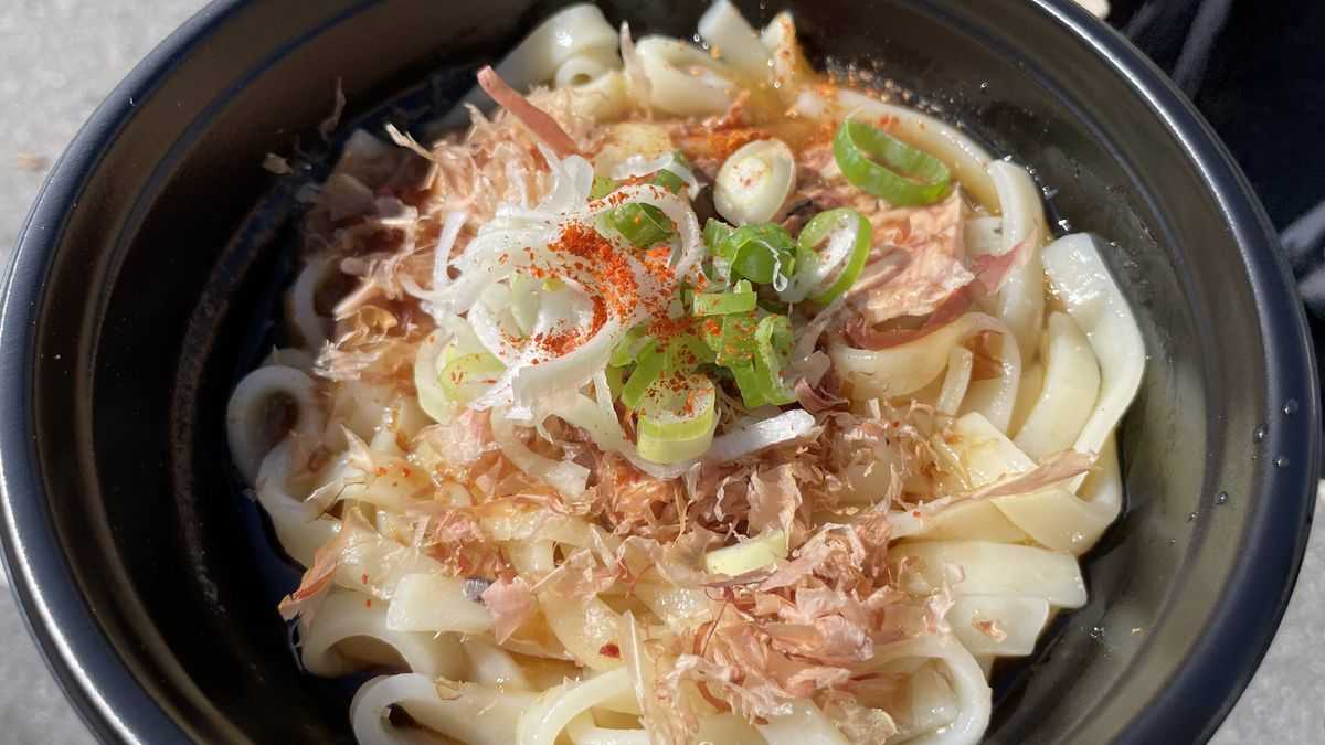 黒い器に入った地獄うどん。太めの麺の上に、かつお節とねぎ、赤い粉がのっている