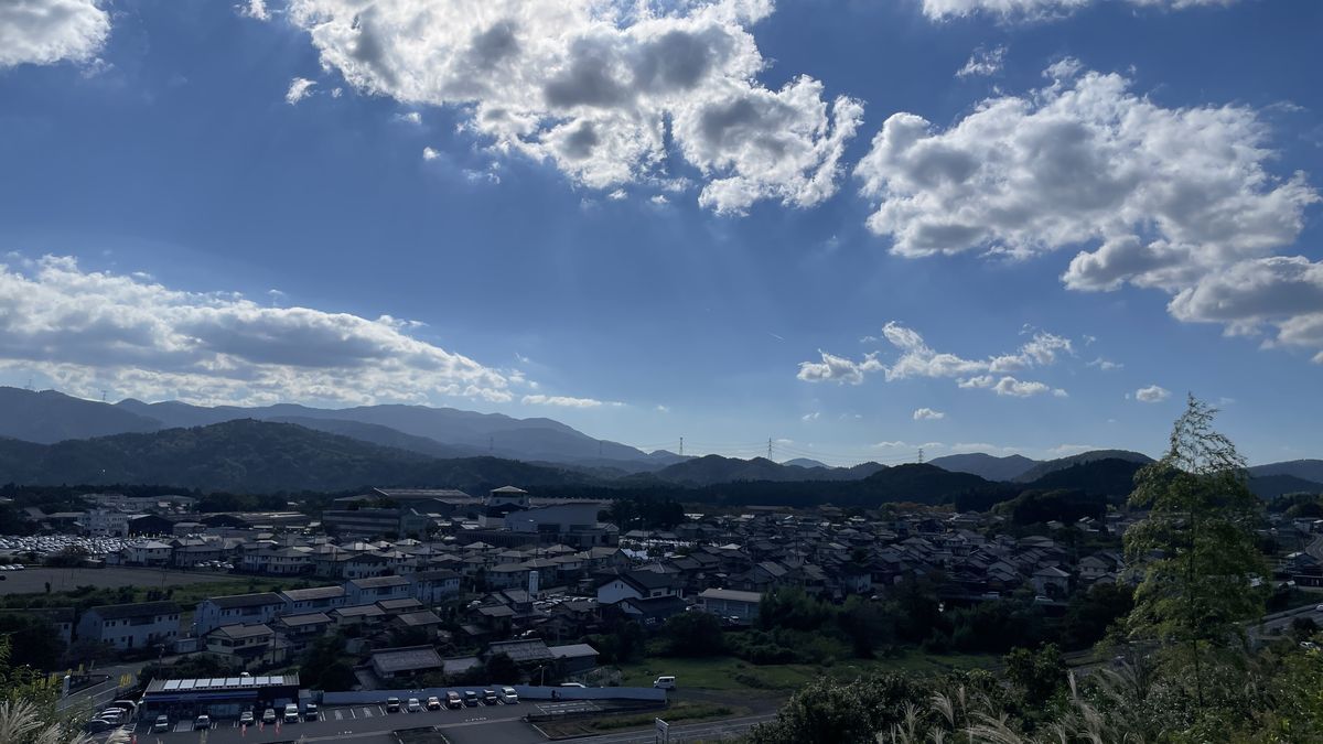 岡山烽火場から見渡した関ケ原の町。家並みの奥に山並みが連なり、青空に大きな雲が浮かんでいる