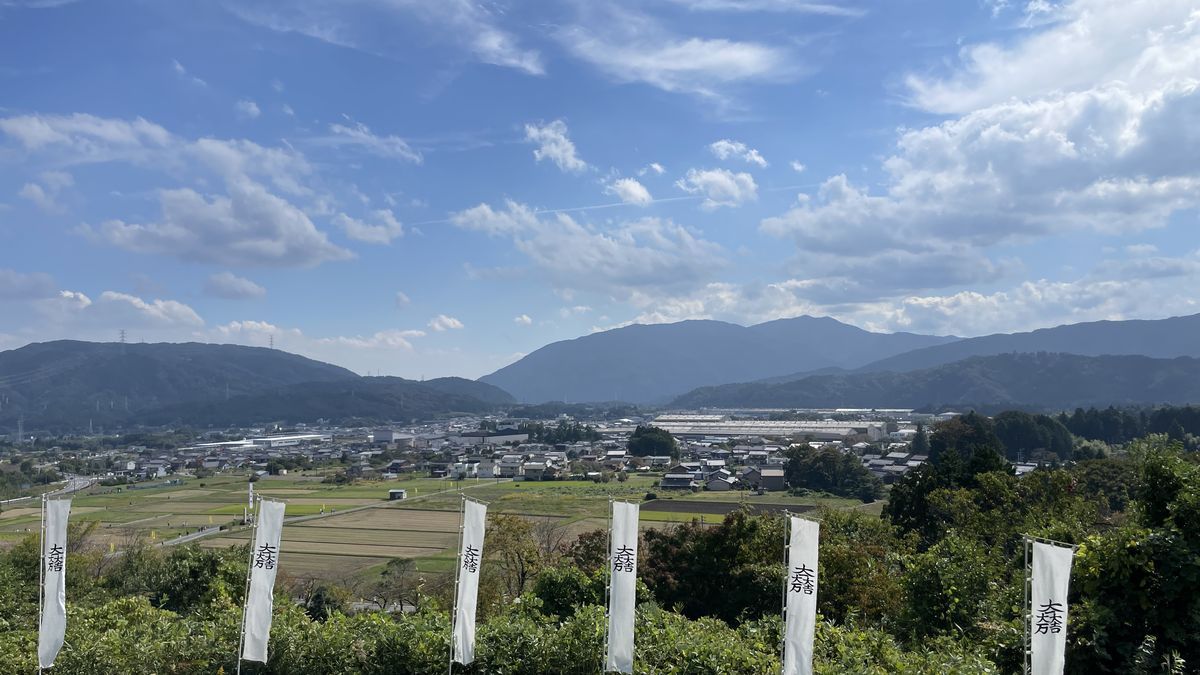 笹尾山から見下ろした関ケ原。手前に白いのぼりが並び、田んぼと町、奥に山並みと青空が広がっている