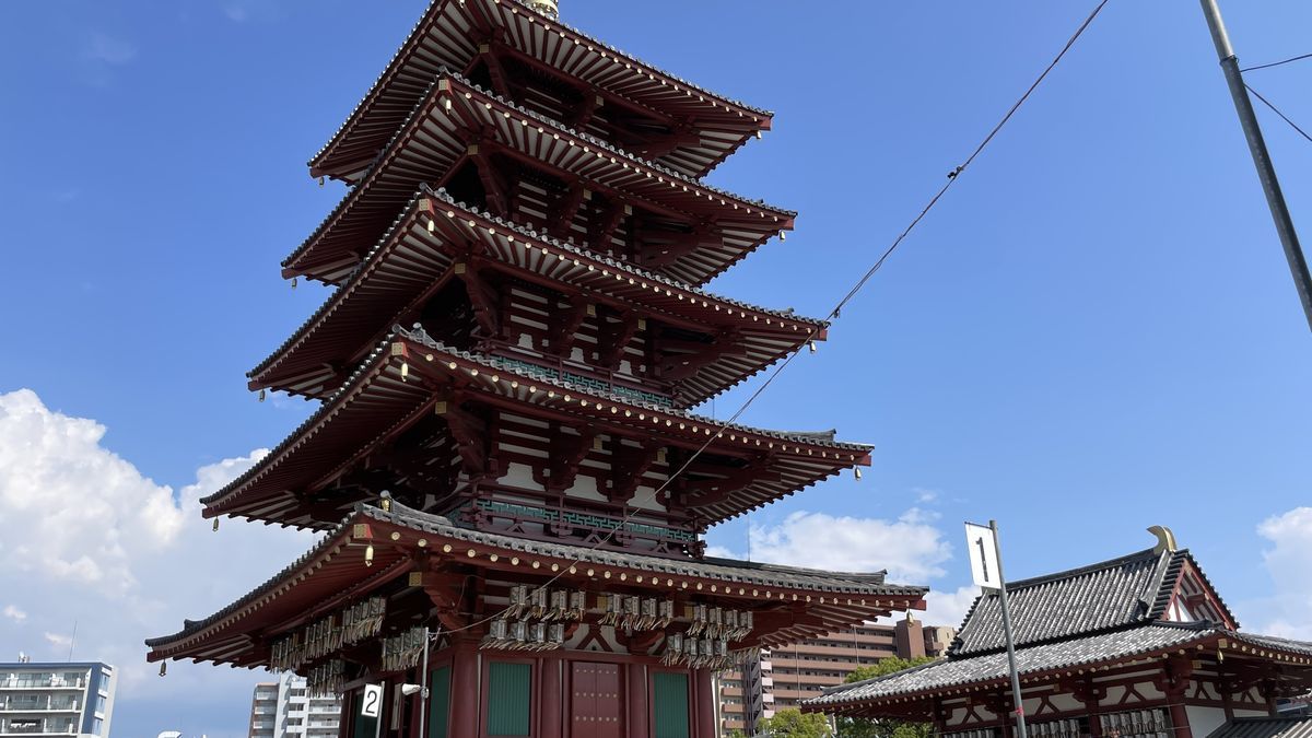 四天王寺の五重塔を見上げた写真。朱色の柱と緑の格子の五重塔が、青空の下に立っている