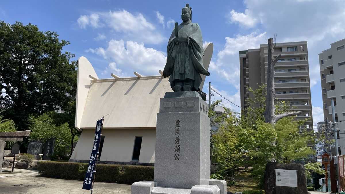 玉造稲荷神社の豊臣秀頼公の銅像。台座に「豊臣秀頼公」と刻まれ、後ろに青空とマンションが見える