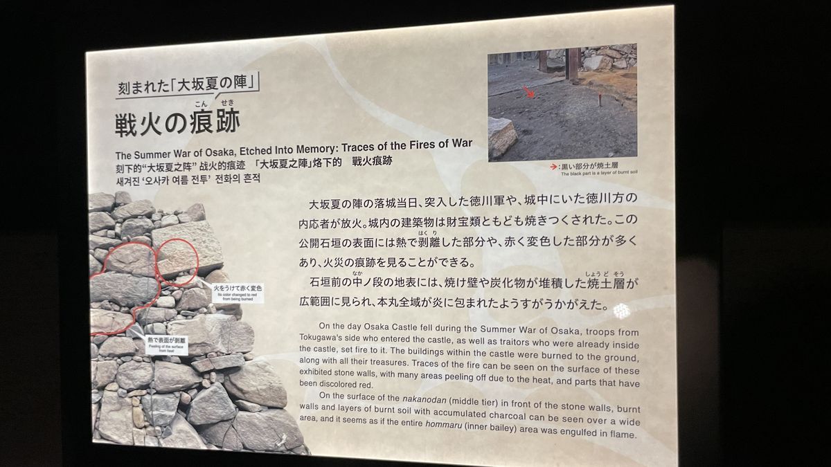 大阪城 豊臣石垣館の説明パネル「戦火の痕跡」。大坂夏の陣の火で赤く変色した石や、熱で表面がはがれた石の場所が、石垣の写真に赤い線で示されている