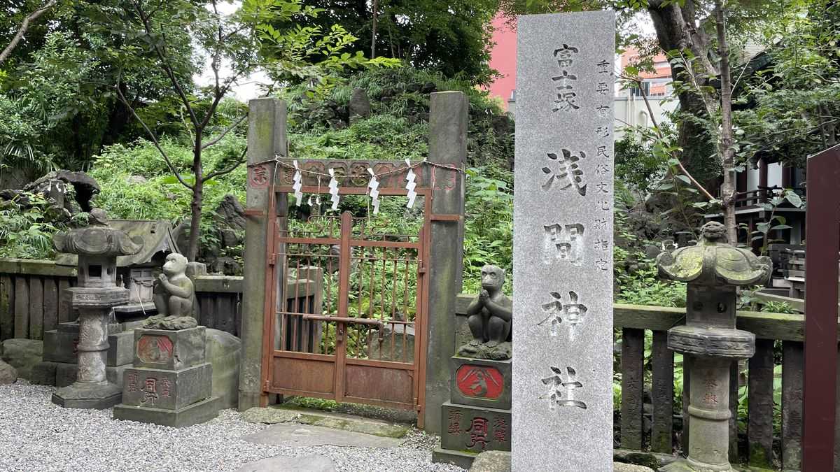 富士塚の入口。閉まった鉄の門の横に「浅間神社」と刻まれた石柱と、猿の石像が立っている