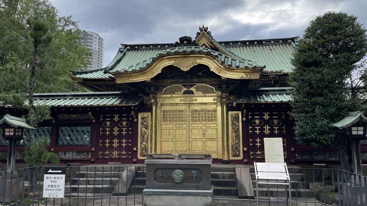 上野東照宮の唐門。金色の門と緑の屋根の前に、「奉納」と書かれた賽銭箱がある