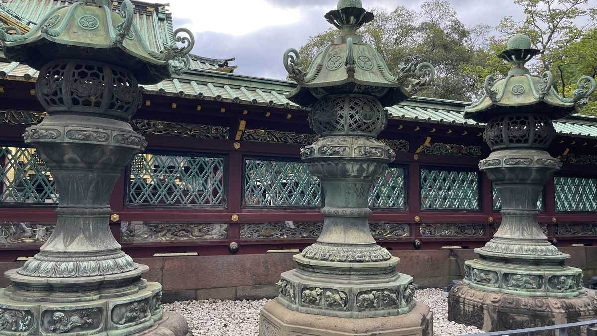 赤い塀と緑の格子の前に並ぶ、3基の銅灯籠